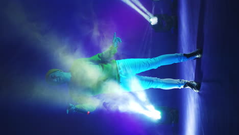 vertical video. incendiary funny singer in yellow clothes dancing and singing with a microphone in neon color. jump and move vigorously. hip-hop and pop artist