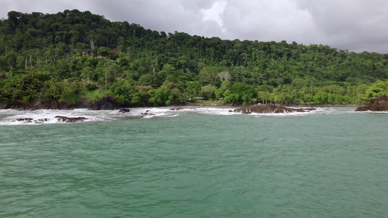 camión aéreo a la derecha del mar turquesa cerca de la costa rocosa y la ladera del bosque en un día nublado en la playa dominicalito, costa rica