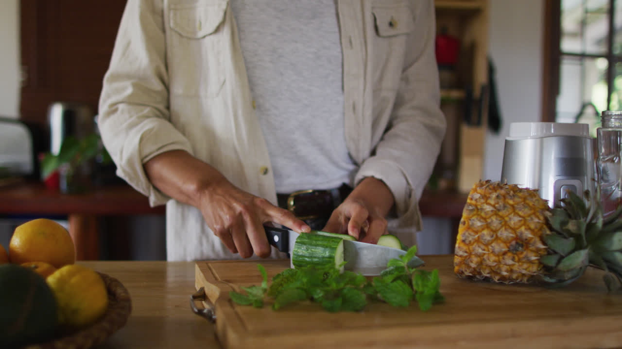 sección media de mujer de raza mixta cortando frutas y verduras en la cocina de la cabaña