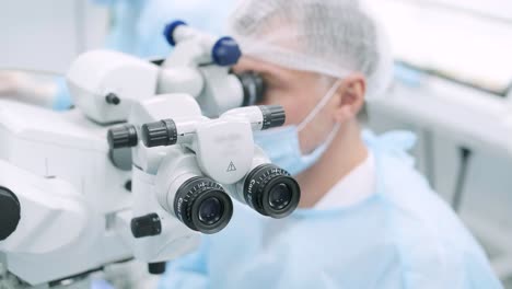 ophthalmological surgery specialist sits in front of microscope performing operation. low angle view on the female doctor conducting high-precision surgery. femto laser assisted cataract surgery. cataract surgery. ophthalmic operation