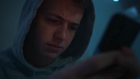 Focus-caucasian-teenage-boy-using-mobile-phone-while-sitting-at-night-in-his-room