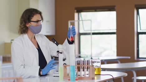 maestra con máscara facial sosteniendo un tubo de ensayo en el laboratorio de la escuela