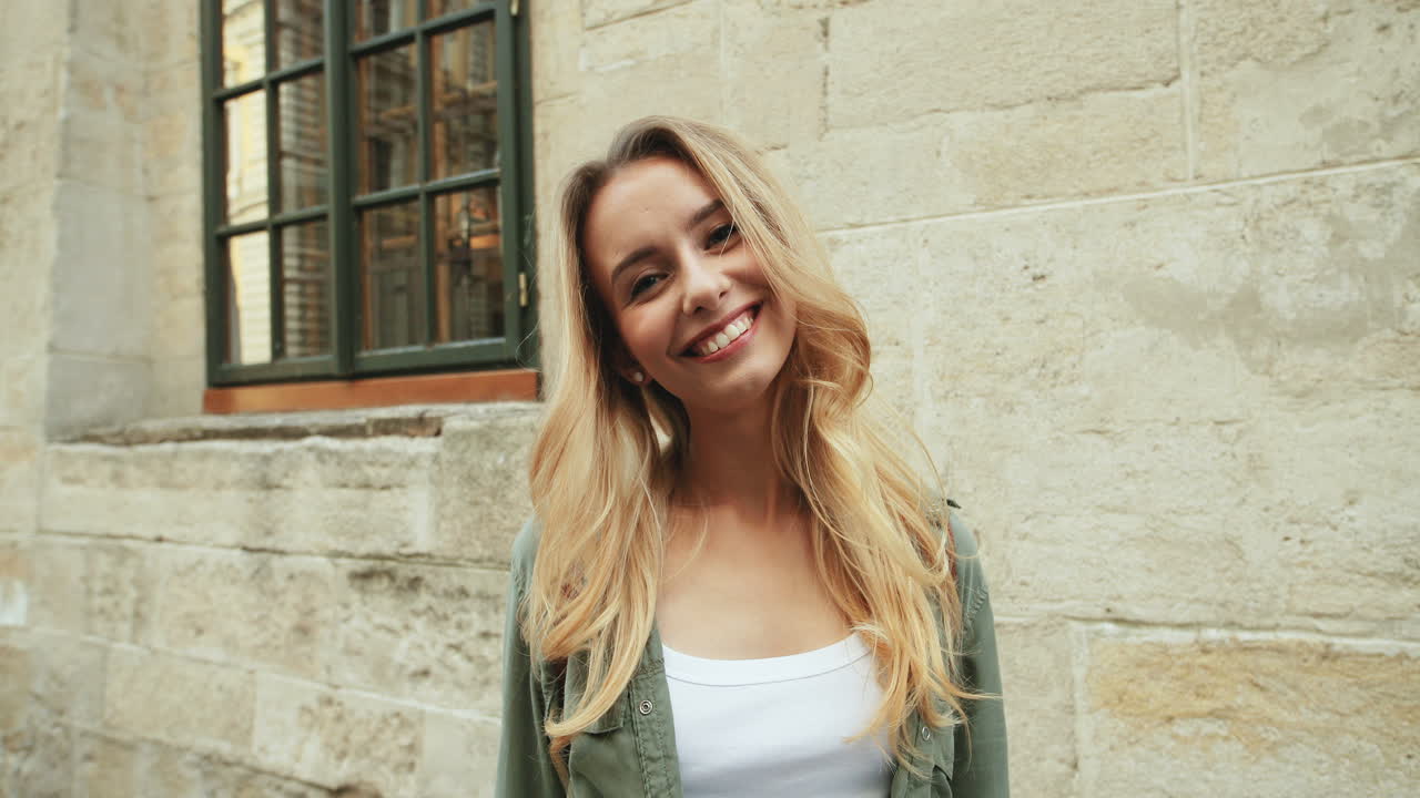 кавказская светловолосая молодая женщина улыбается в камеру, стоя на улице