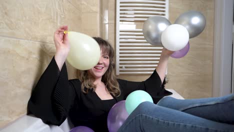 mujer joven sentada en la bañera tirando globos en el baño