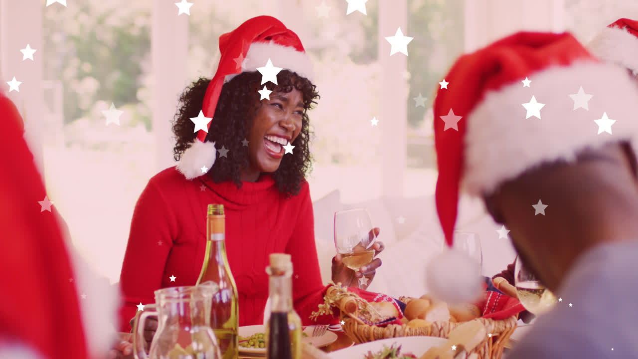 animación de estrellas cayendo sobre una feliz familia afroamericana con sombreros de papá noel y cenando