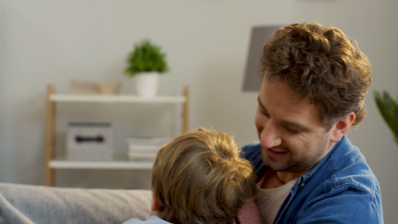 cerca del alegre padre e hijo divirtiéndose en el sofá de la sala de estar, peleando con almohadas, haciéndose cosquillas y riendo