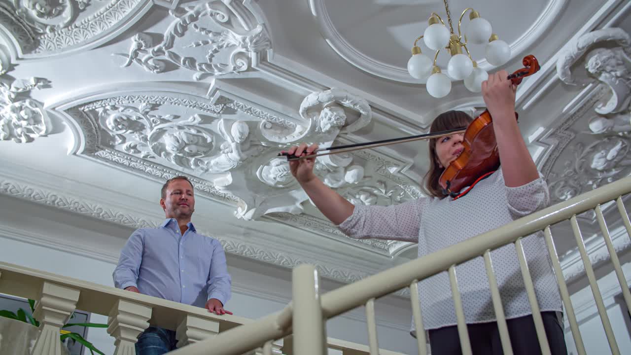바이올리니스트가 연주하는 동안 우아한 여성이 계단을 올라가고 있어요. 낮은 앵글입니다.