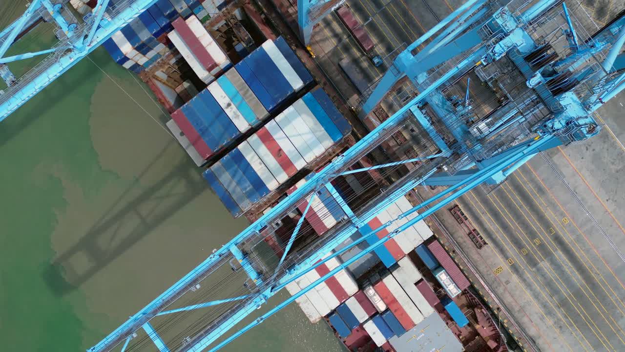 gantry cranes moving containers from a docked cargo ship, illustrating global shipping and supply chain logistics. Perfect aerial view drone top down Above view