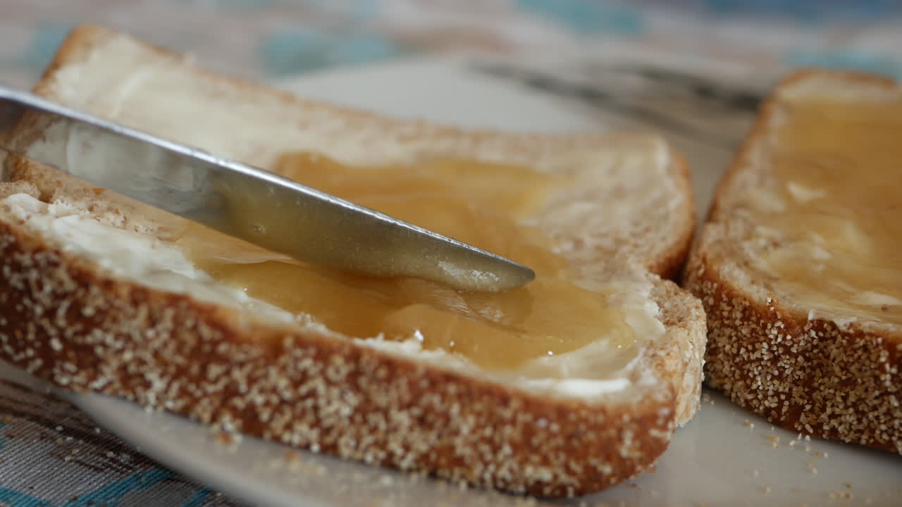 Silver knife spreads and puts on honey on buttered bread slice