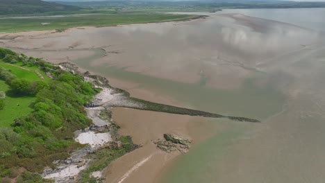 High-altitude-view-of-manmade-stone-structure-Walduck's-Wall-and-receding-tide-with-cloud-reflections-on-water-on-bright-spring-day-at-Jenny-Brown's-Point,-Silverdale,-Lancashire,-England,-UK