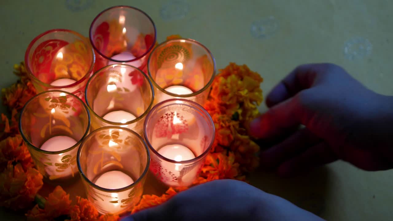Hindu festival of lights, Dusshera and Diwali preparation and celebration ingredients- decorative painted glasses with t-candles and flowers being added by a human hand