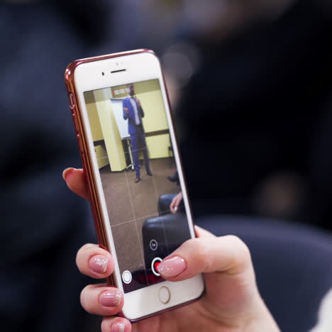 woman is watching the part of the video conference of the speaker on her smartphone. phone in female's hands on the blurred background.