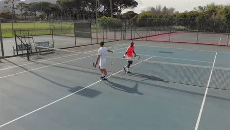 diverse male tennis players holding rackets and shaking hands at court