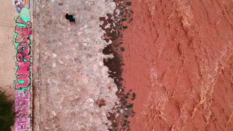 dolly in top view of a young couple walking along a rocky path beside the murky mapocho river, deep brown in color due to sediment composed of soil