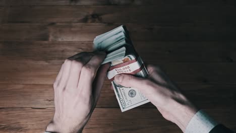 las manos masculinas sostienen tres pilas de billetes de 10.000 dólares en un fondo de madera.