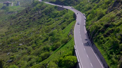 Downward aerial shot of a winding mountain road with sparse cars and lush vegetation on the steep slopes