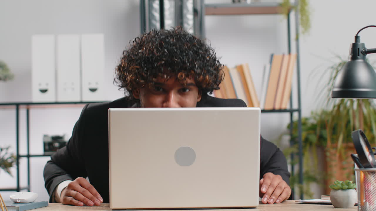Office businessman hiding behind laptop computer making funny silly face fooling around disrespect