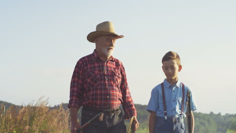 Caucasian-grandfather-and-his-little-grandson-walking-together-while-holding-fishing-rods-in-the-morning