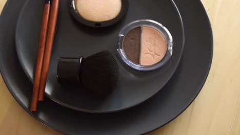 minimal concept background with make up, brushes and powders, on a grey plate, rotating on a wooden table