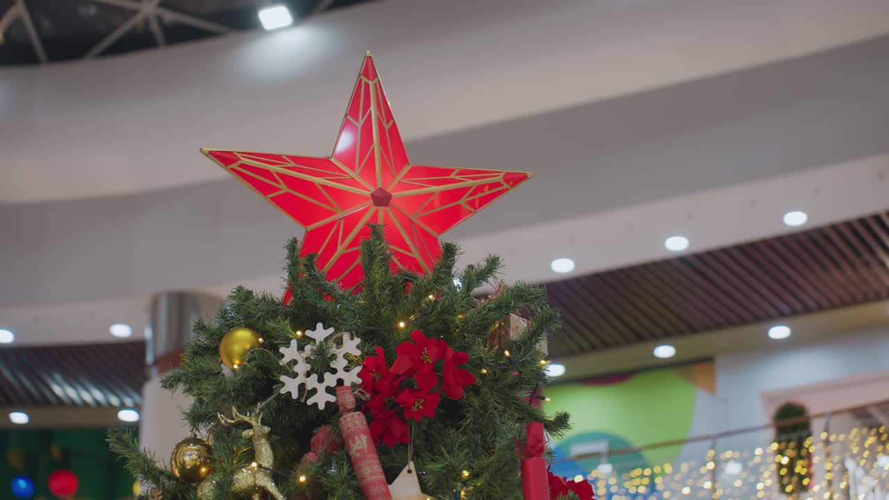 Close-up of beautifully decorated Christmas tree with glowing red star topper, golden ornaments, snowflakes, poinsettias, and festive decorations adorn lush green branches