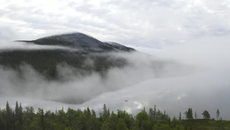 aerial shot of a misty landscape with lake and flying closer to a small rowing boat with a person on it