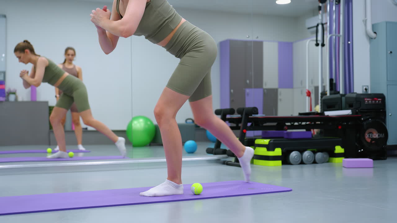 ejercicio de flexibilidad de las piernas en progreso con el instructor de gimnasia observando, mujer realizando una agachada controlada con enfoque en el equilibrio y la fuerza del núcleo, características de fondo equipo de gimnasio
