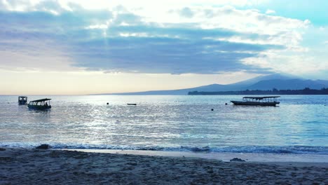 Early-morning-on-the-tropical-sunset,-mountains-covered-in-the-fluffy-clouds,-and-fishing-boats-floating-in-the-calm-sea