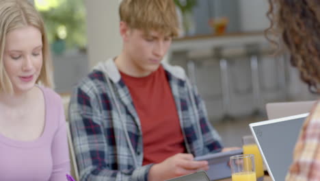 happy diverse group of teenage friends studying at table with tablets at home, slow motion