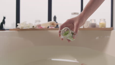 vue rapprochée des mains de la femme versant des sels de bain et des fleurs dans l'eau de la baignoire