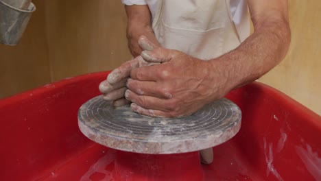 senior caucasian man wearing apron and forming pottery in his workshop