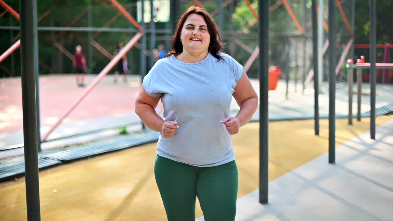 Donna in sovrappeso con una t-shirt grigia e leggings che si allena su un campo sportivo in un parco per perdere peso. Stile di vita fitness