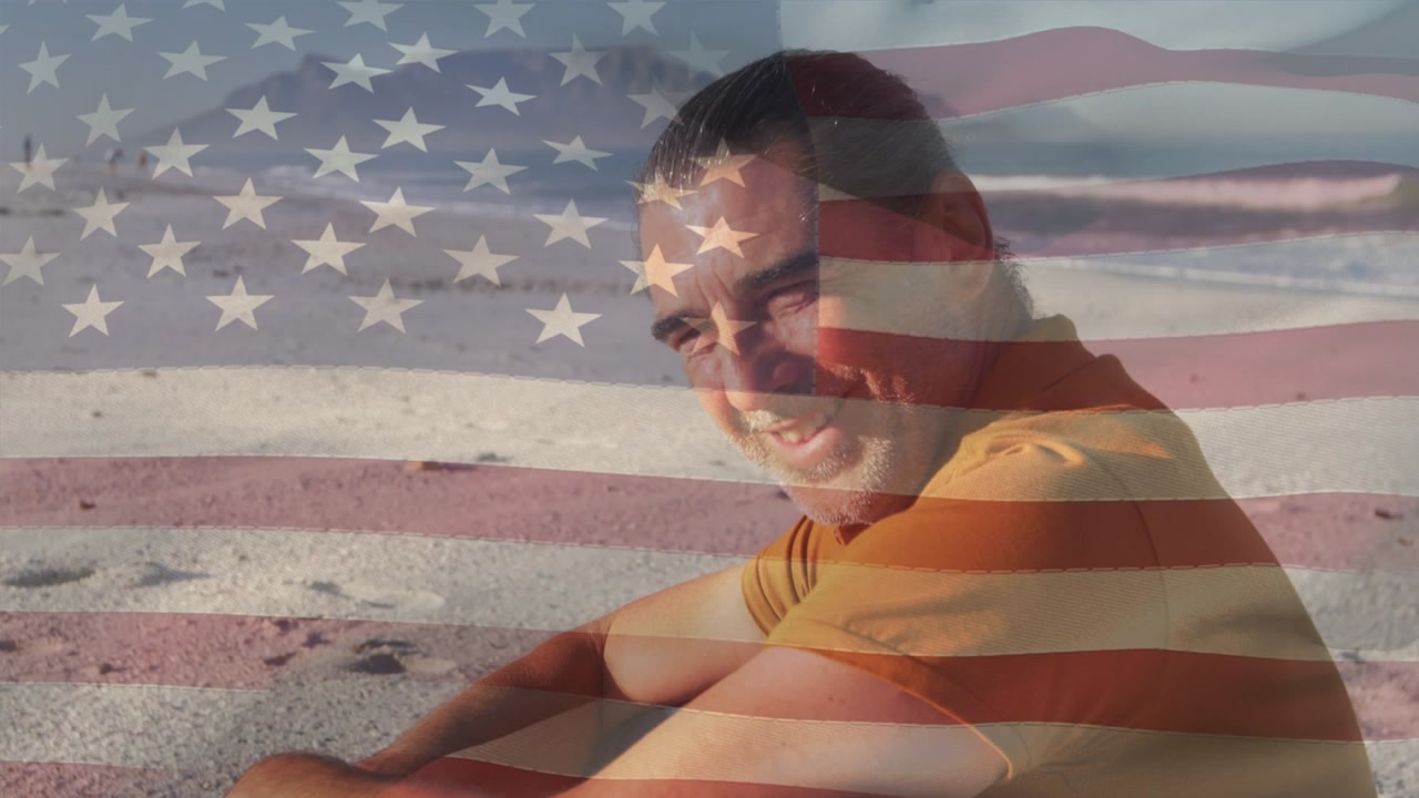 Animation of flag of united states of usa over happy african american man on beach