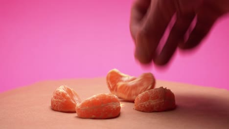 Hand-puts-ripe-peeled-mandarins-on-rotate-pink-and-old-paper-background-4k-video-with-color-correction