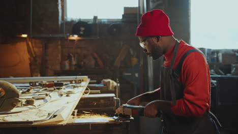 african american blacksmith polishing metal with angle grinder at workbench