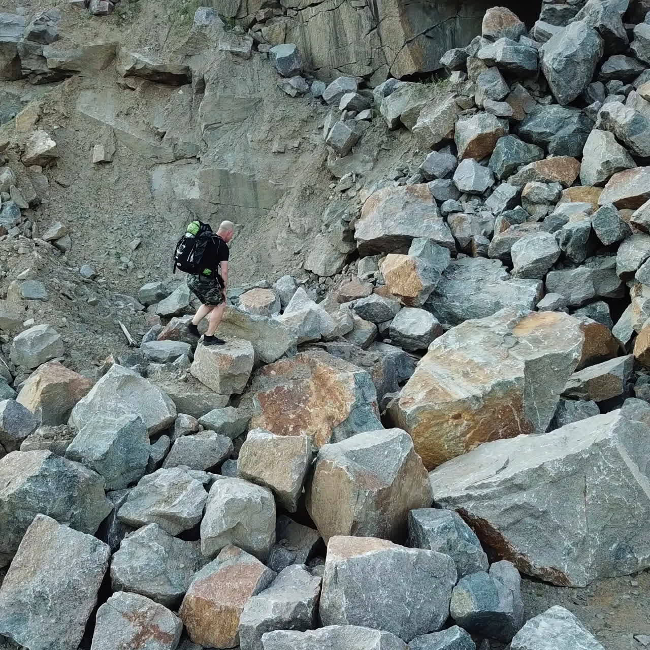 Natural background of a rocky place and a tourist climbing in summer. Hiker walking over the large pile of stones in a mountainous area.