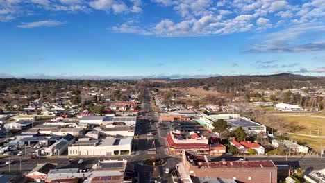 drone camera glides above glen innes town center, revealing urban streets, commercial buildings, and residential areas under bright daylight with scattered clouds