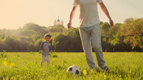 a young father in a white t-shirt with two sons playing football on the grass at sunset in the sun in slow motion