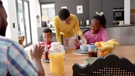 Padres-Afroamericanos-Con-Hijo-E-Hija-Desayunando-En-La-Mesa-De-La-Cocina,-Cámara-Lenta