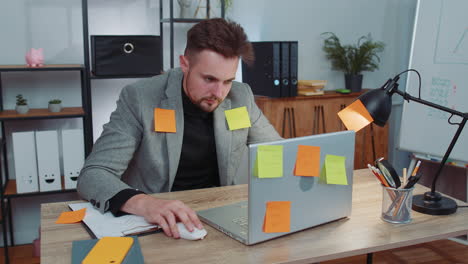 tired sad exhausted businessman working on laptop at office with many sticker tasks, panic attack