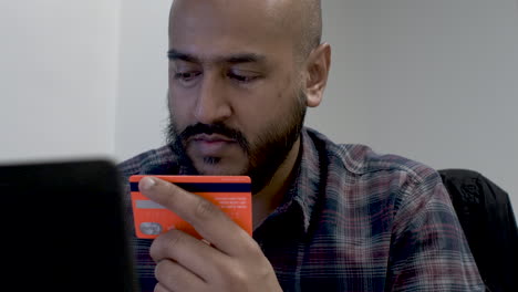 a close up shot of an indian man enthusiastically entering his credit card details as he is excited to complete an online e-commerce purchase