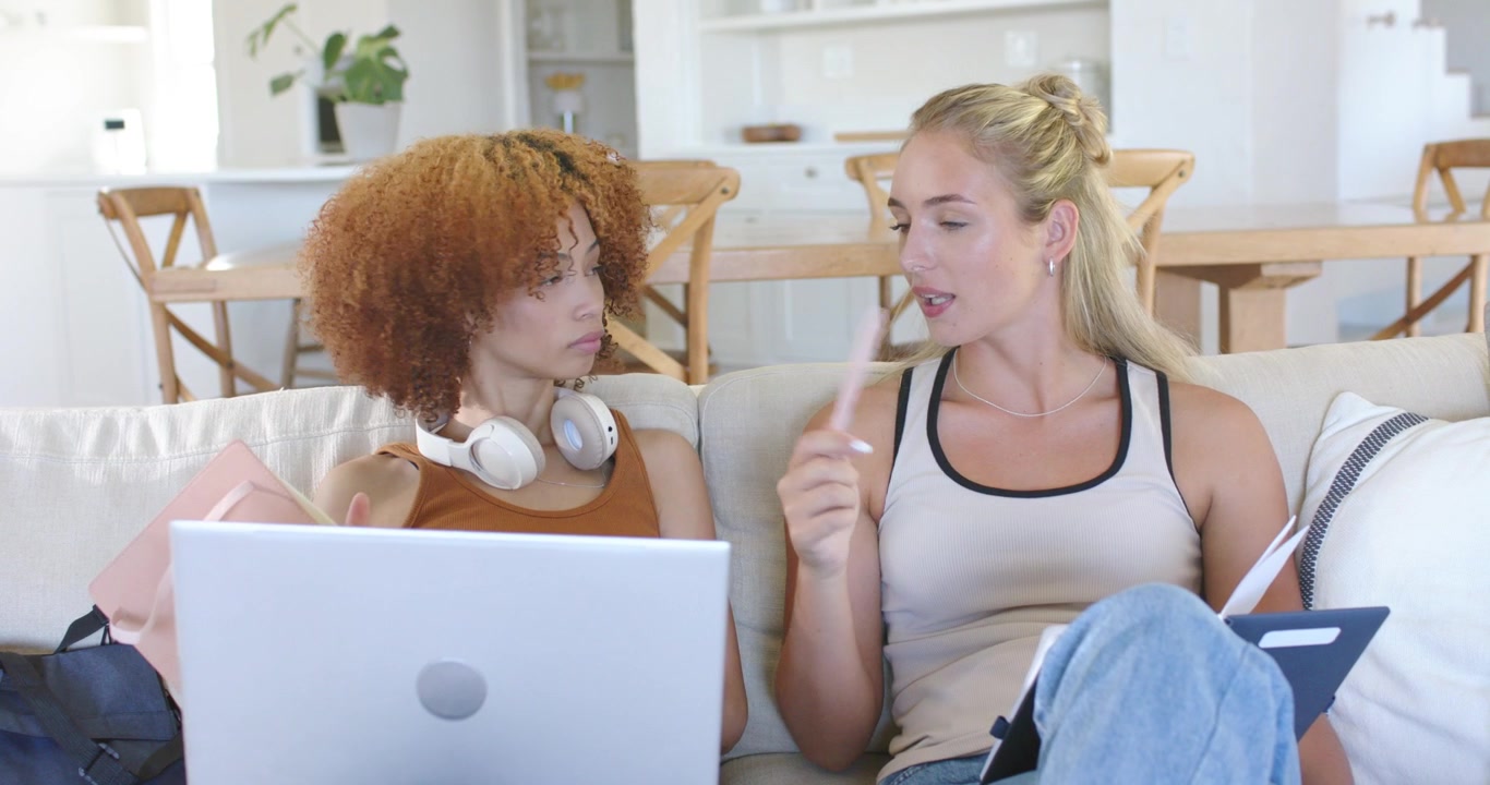 Donne sedute sul divano, quella a destra che indica con una penna, esortando quella a sinistra che digita sul laptop e sposta una cartella.