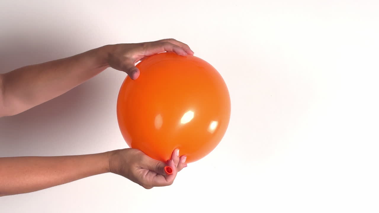 Manos desinflando un globo naranja sobre un fondo blanco