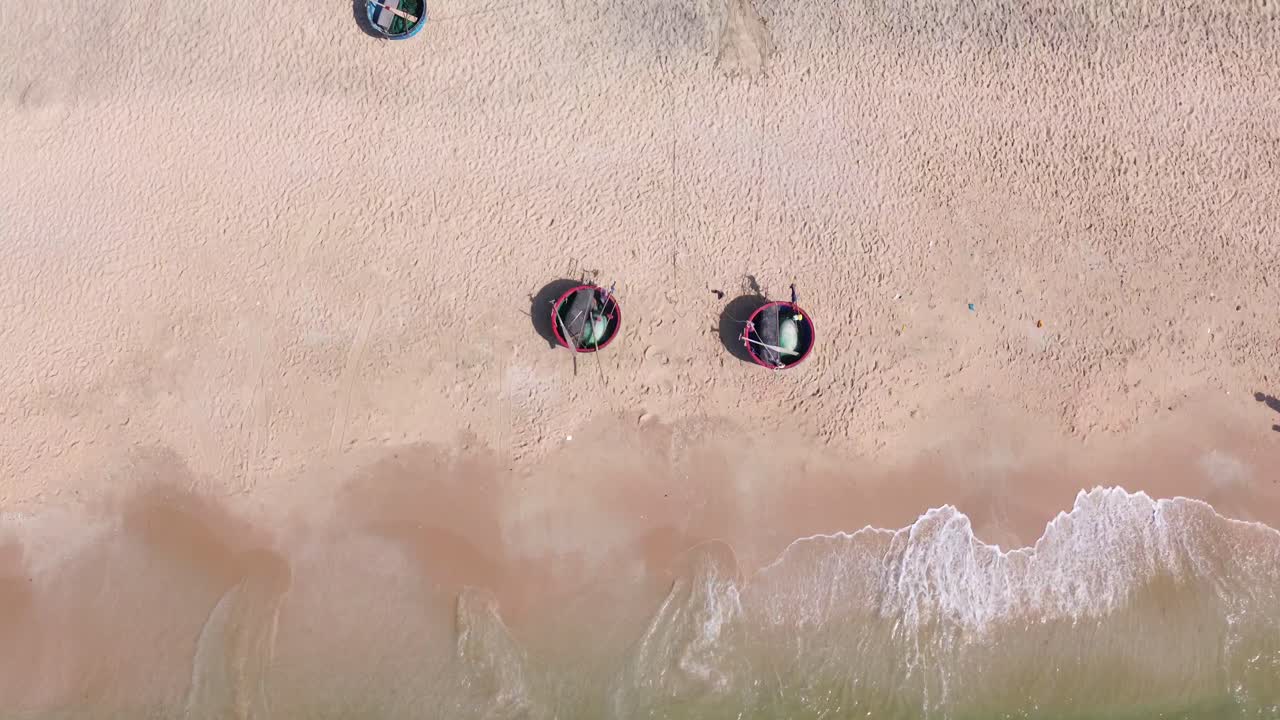 Drone moving top-down from sand beach towards shoreline and gentle waves in Mui Ne, Vietnam.