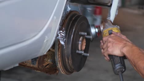 hands holding a grinder with steel brush cleaning the wheel hub from rust then the right hand turns the hub to reposition, , automotive shop, thailand