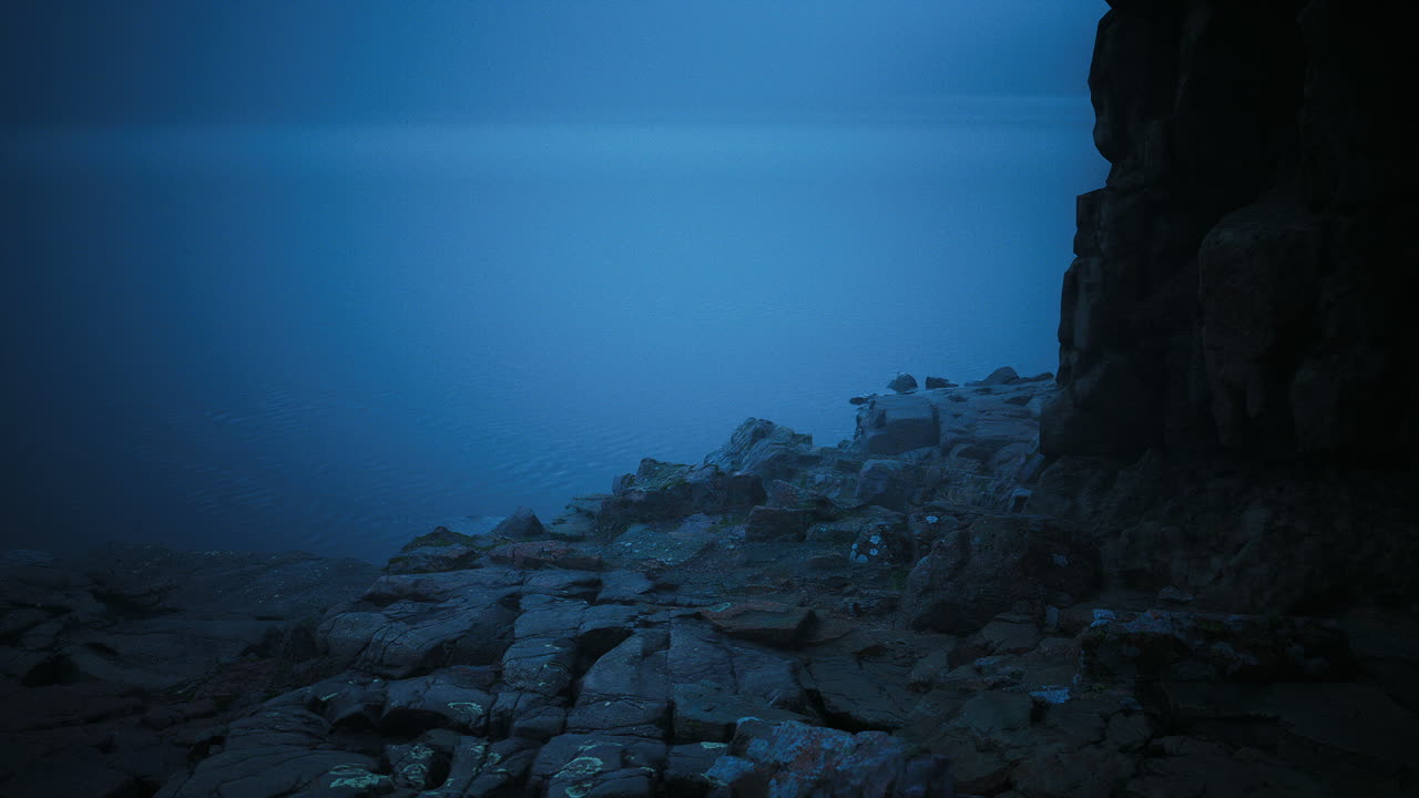 Misty coastal landscape at dawn with rocky shoreline and calm waters