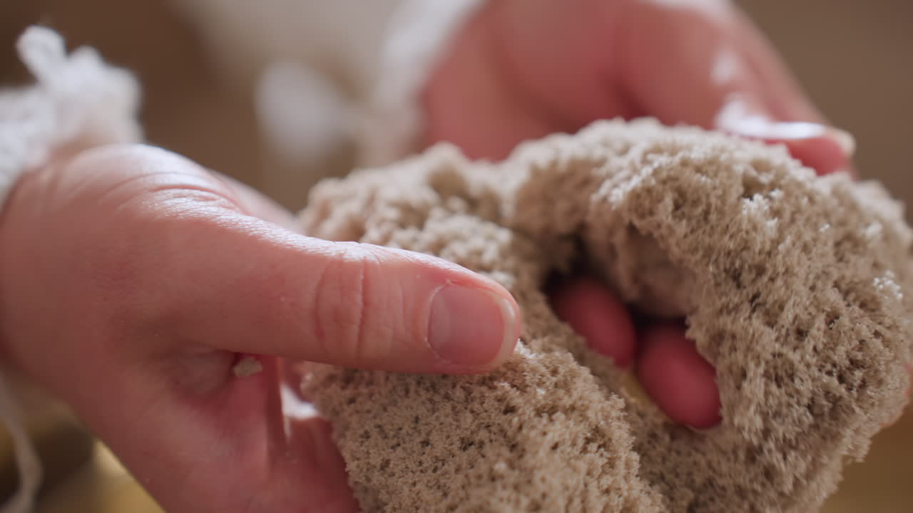 Close up of individual hands gently lifting soft textured soil mold during calming sensory therapy session, capturing moment of tactile interaction in peaceful indoor setting with warm light