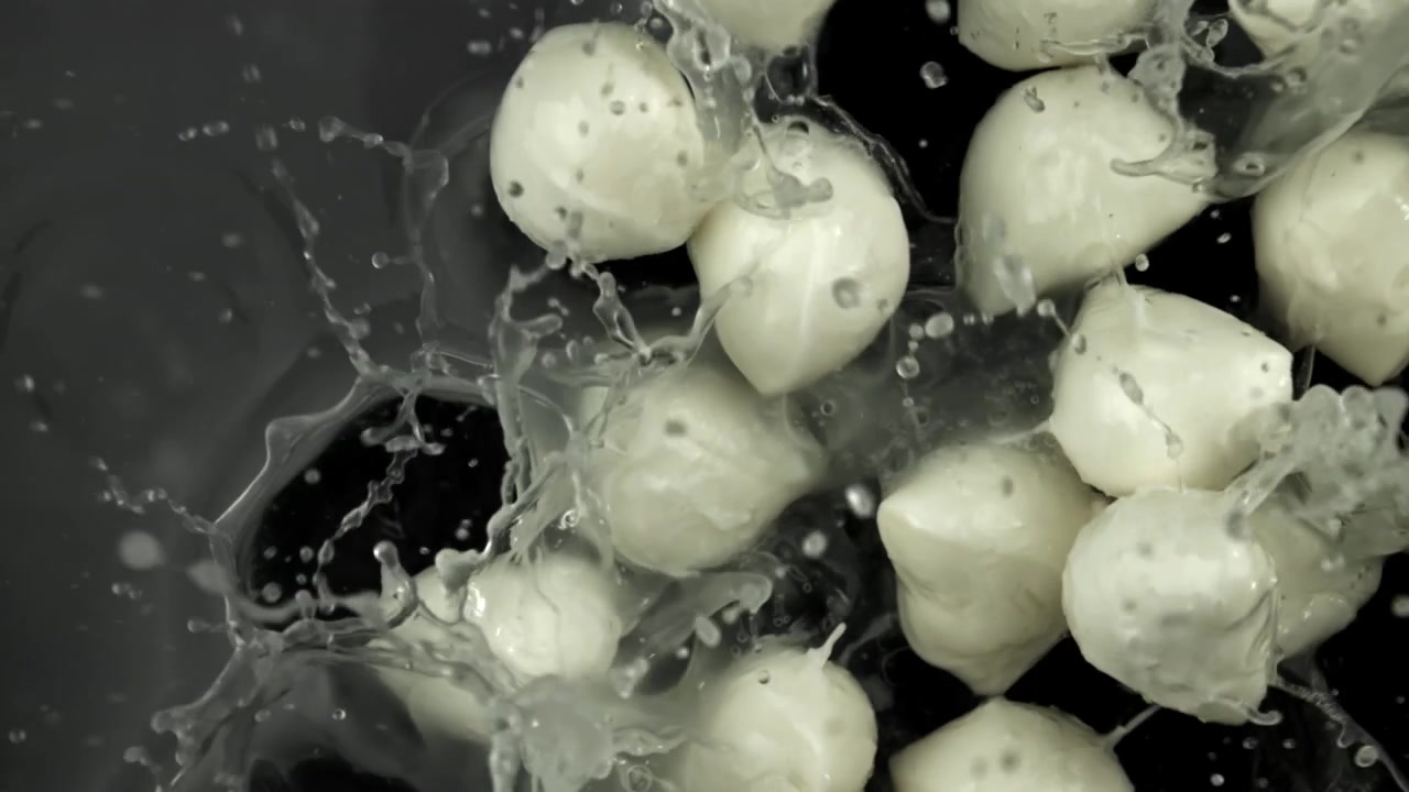 Mozzarella fresca che schizza nell'acqua su sfondo scuro