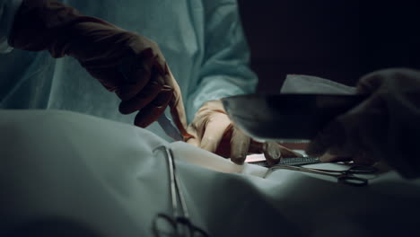 las manos del cirujano haciendo una incisión con un bisturí en una sala oscura del hospital de cerca.