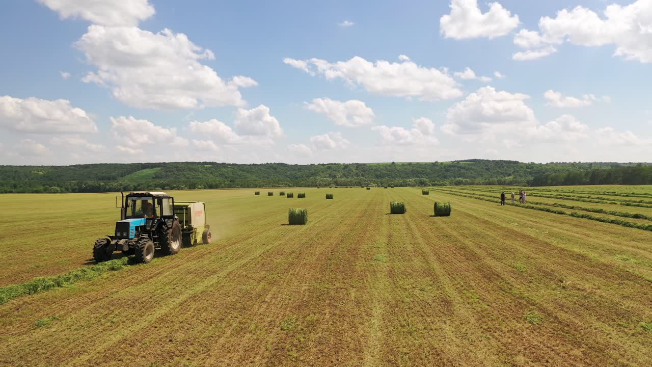 Side view of an agricultural tractor working in the field. Seasonal works for harvesting grass for farming outdoors. Tractor in field press grass into bales.