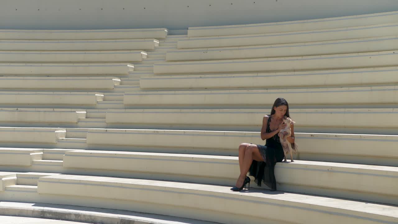 Sexy Woman in a Black Dress Having Fun With Her Kokoni Dog Puppy on Amphiteathre Stands, Tala Village, Cyprus